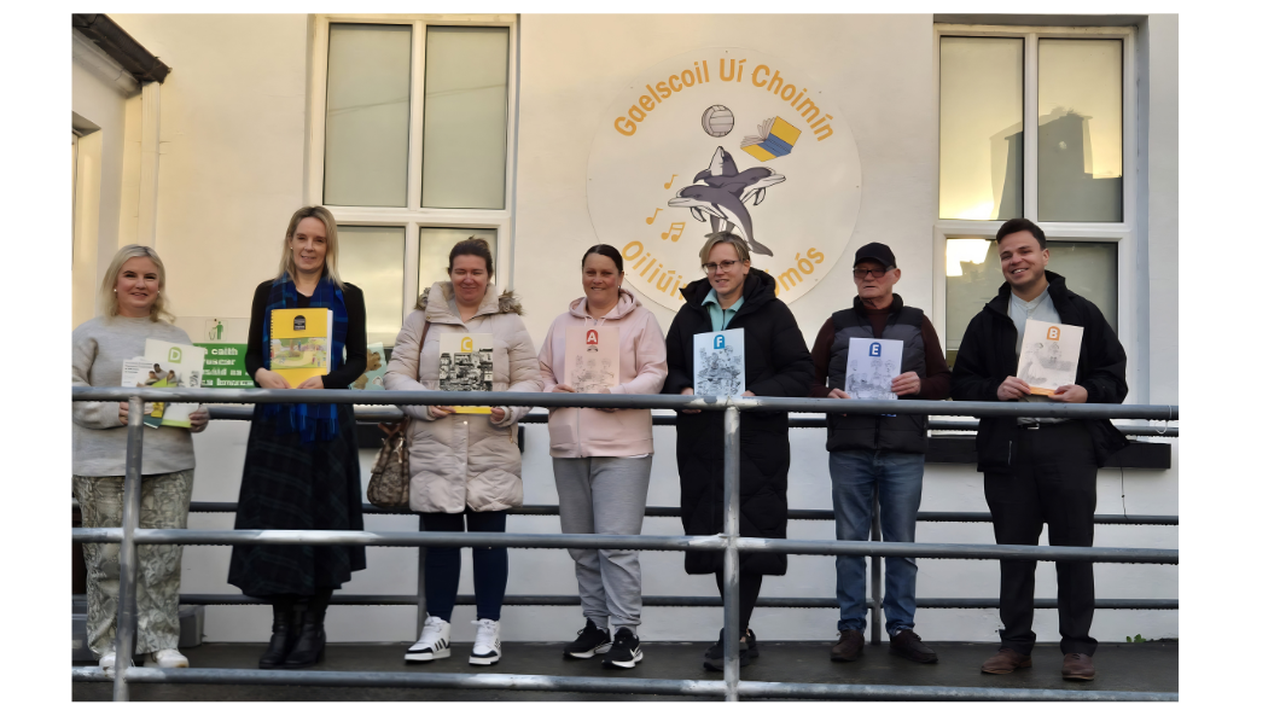 Seven people standing in a row outside a building, each holding a different colored certificate, with 